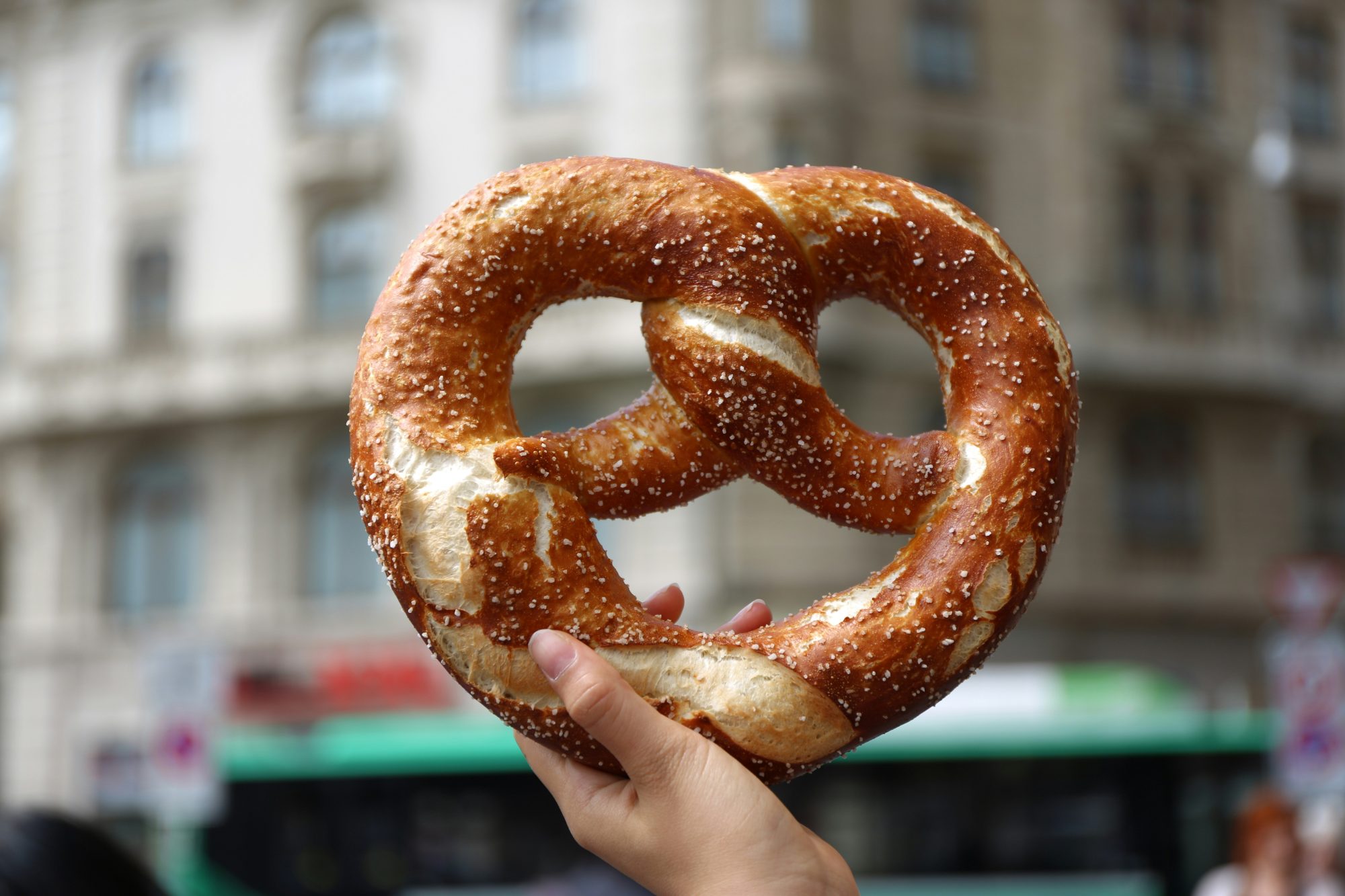 Large soft Brezels being held up in a busy street